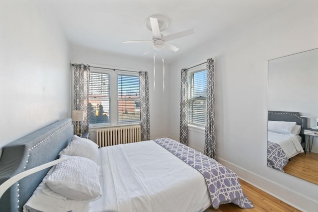 bedroom featuring multiple windows, radiator heating unit, baseboards, and wood finished floors