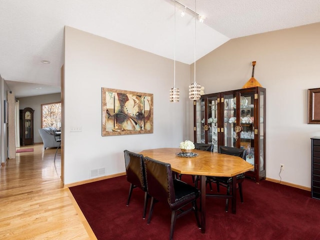 dining space featuring wood finished floors, baseboards, visible vents, lofted ceiling, and a chandelier