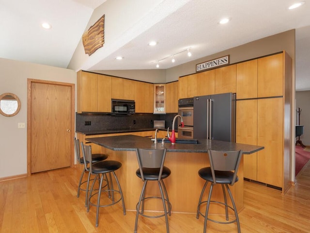 kitchen with a sink, dark countertops, light wood-style floors, and stainless steel appliances