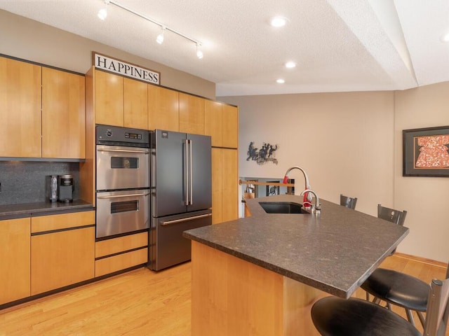 kitchen featuring light wood-type flooring, a kitchen bar, appliances with stainless steel finishes, a textured ceiling, and a sink