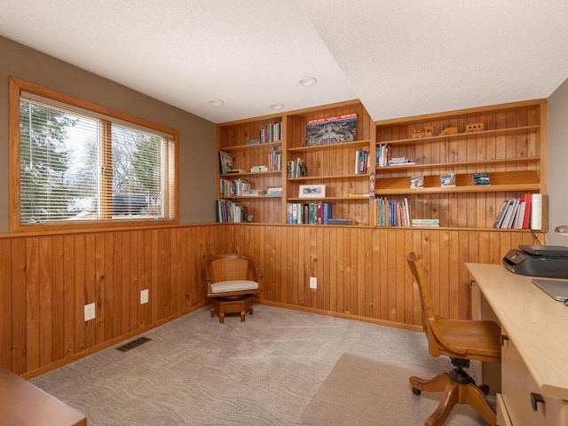 carpeted office space with visible vents, built in features, wood walls, wainscoting, and a textured ceiling