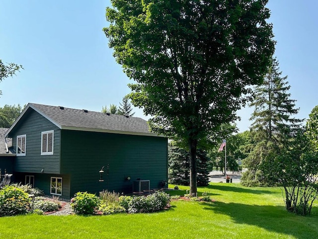 view of side of home with central AC unit, a lawn, and a shingled roof