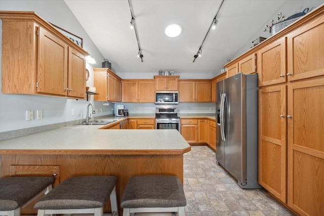 kitchen with a peninsula, a sink, light countertops, appliances with stainless steel finishes, and a kitchen breakfast bar