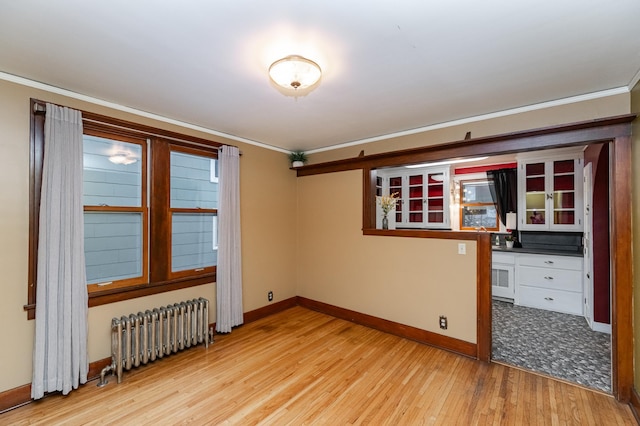 empty room with baseboards, ornamental molding, light wood finished floors, and radiator