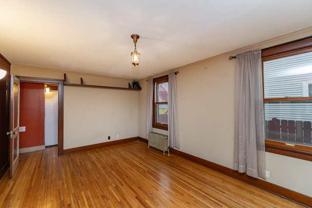 empty room with baseboards, light wood finished floors, and radiator heating unit