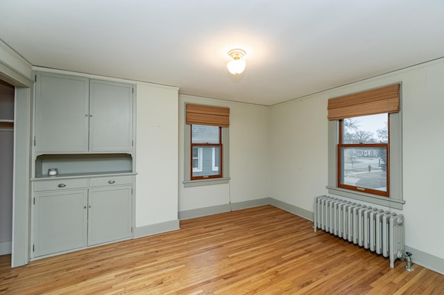 unfurnished room featuring baseboards, radiator, and light wood-style floors