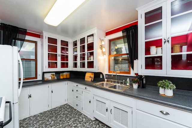 kitchen featuring freestanding refrigerator, a sink, white cabinets, and dark countertops