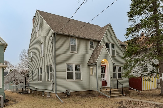 rear view of house featuring roof with shingles, fence, and a chimney