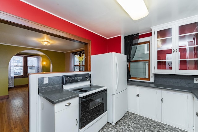 kitchen featuring arched walkways, white cabinetry, dark countertops, and white appliances