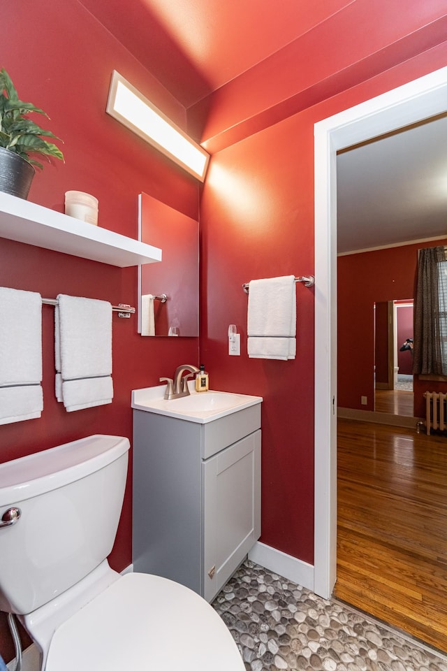 bathroom featuring radiator heating unit, vanity, baseboards, and toilet