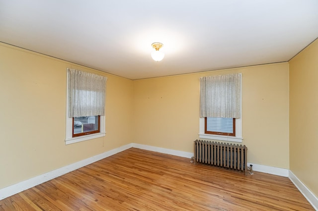 empty room with light wood-style floors, radiator, and baseboards