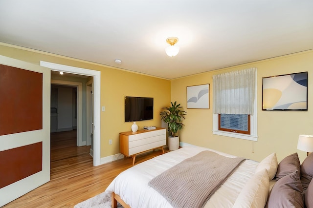 bedroom featuring light wood-style floors, ornamental molding, and baseboards