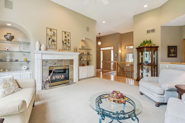 carpeted living room featuring visible vents, built in shelves, ceiling fan, and a tiled fireplace