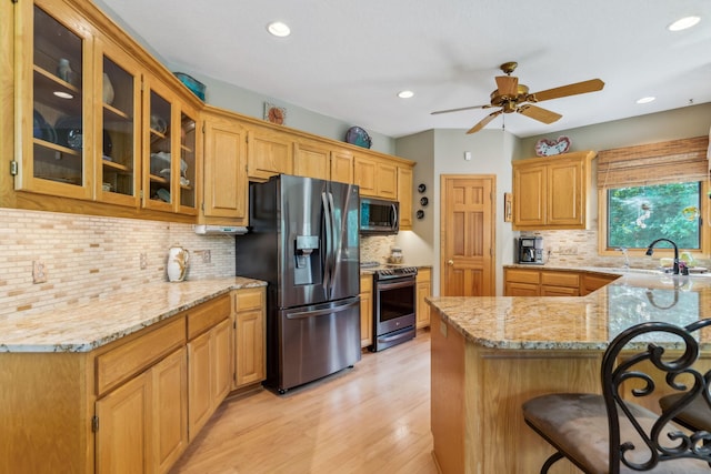 kitchen with light stone counters, a ceiling fan, a sink, stainless steel appliances, and glass insert cabinets