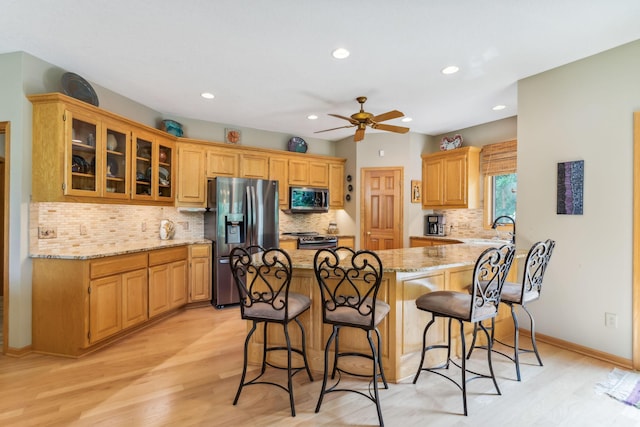 kitchen featuring a kitchen bar, light stone counters, stainless steel appliances, a ceiling fan, and a sink