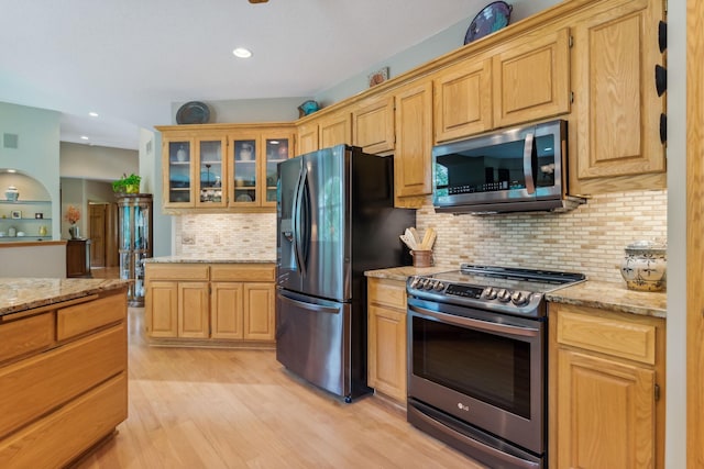 kitchen featuring light stone counters, glass insert cabinets, light wood-type flooring, and appliances with stainless steel finishes