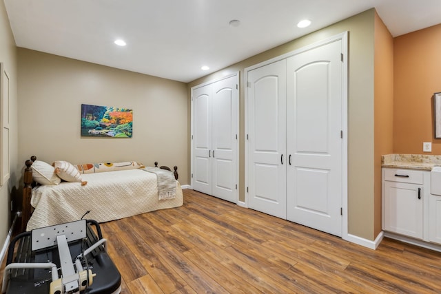 bedroom featuring recessed lighting, wood finished floors, baseboards, and two closets