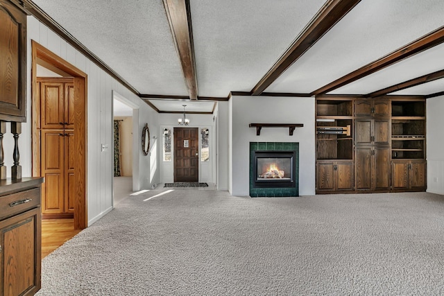 unfurnished living room featuring beamed ceiling, ornamental molding, light colored carpet, and a textured ceiling