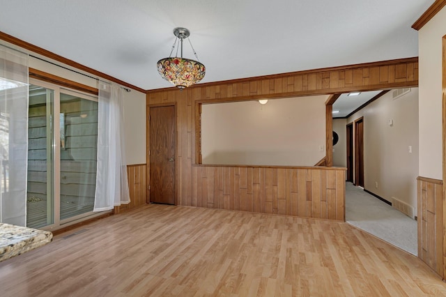 empty room with crown molding, visible vents, and wood walls