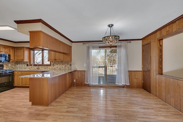 kitchen featuring a wainscoted wall, wood walls, a peninsula, black appliances, and a sink