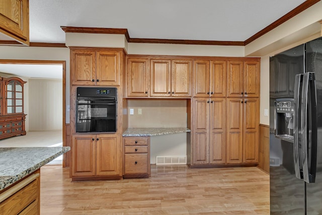 kitchen featuring visible vents, light wood finished floors, built in study area, black appliances, and crown molding