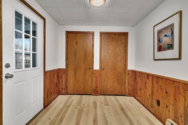 interior space featuring a wainscoted wall, wooden walls, baseboard heating, and light wood finished floors