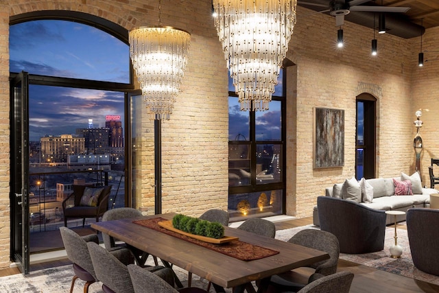 interior space with ceiling fan with notable chandelier, a high ceiling, wood finished floors, and brick wall