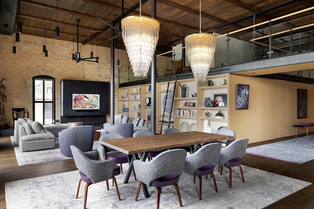 dining room with brick wall, hardwood / wood-style floors, a towering ceiling, and an inviting chandelier