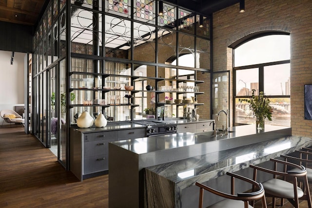 bar with range with gas stovetop, dark wood-style floors, brick wall, and a sink