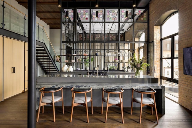 bar with wood finished floors, wet bar, brick wall, and a towering ceiling