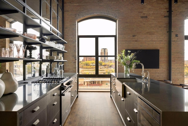 kitchen featuring dark wood-type flooring, open shelves, a sink, brick wall, and dark brown cabinets