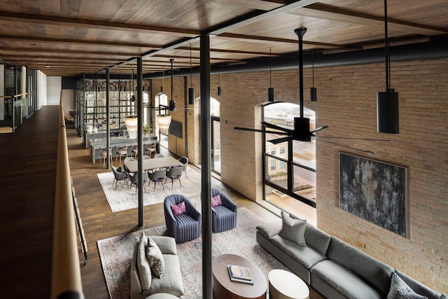 unfurnished living room with a ceiling fan, a high ceiling, wood finished floors, and brick wall