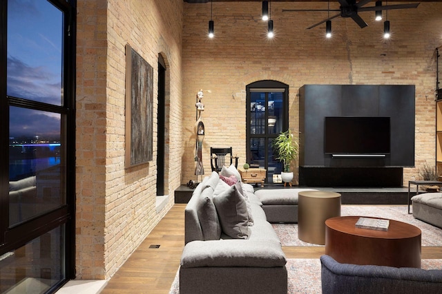 living room with a towering ceiling, brick wall, ceiling fan, and wood finished floors