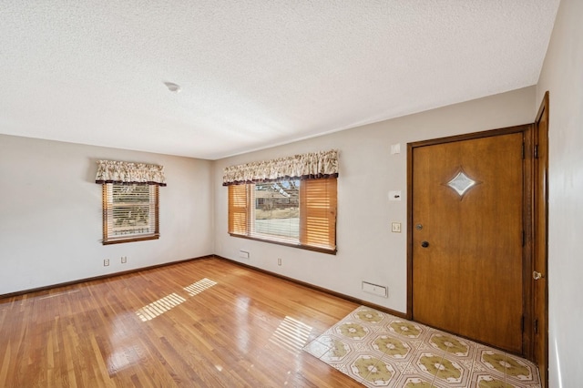 entryway with light wood finished floors, a textured ceiling, and baseboards