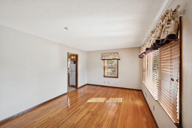 empty room with baseboards, light wood finished floors, and a textured ceiling