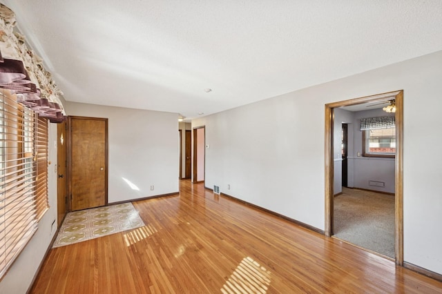 unfurnished living room featuring light wood finished floors, visible vents, a textured ceiling, and baseboards