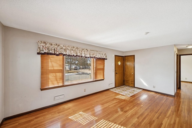 empty room with a textured ceiling, baseboards, and hardwood / wood-style flooring