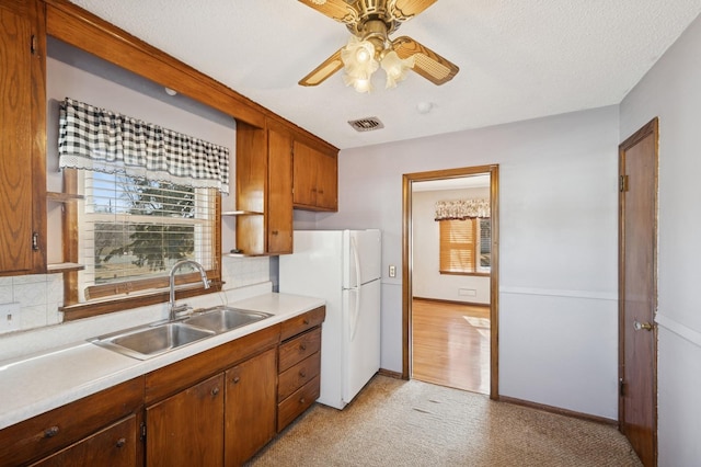 kitchen with a ceiling fan, a sink, backsplash, freestanding refrigerator, and light countertops