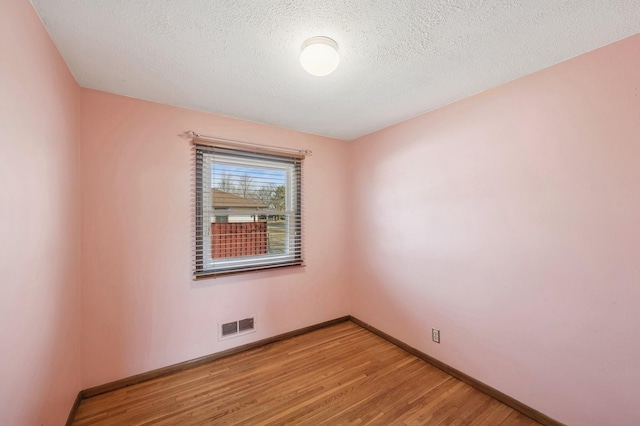 unfurnished room featuring a textured ceiling, light wood-style floors, visible vents, and baseboards