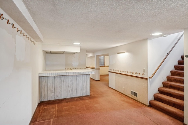 kitchen with visible vents, a textured ceiling, a peninsula, light countertops, and light colored carpet