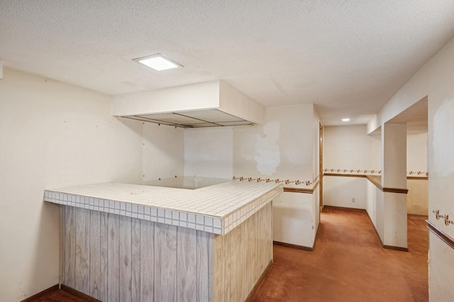 kitchen featuring a peninsula, a textured ceiling, baseboards, and carpet floors