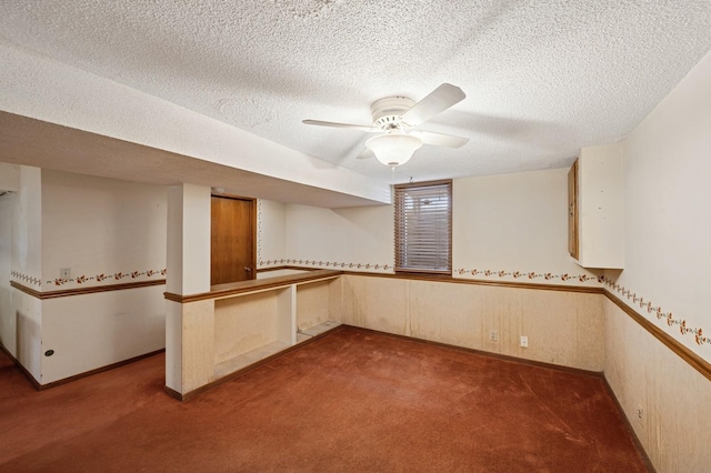 interior space with a wainscoted wall, a textured ceiling, and ceiling fan