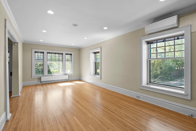 unfurnished living room featuring radiator heating unit, a wall unit AC, crown molding, baseboards, and light wood-style flooring