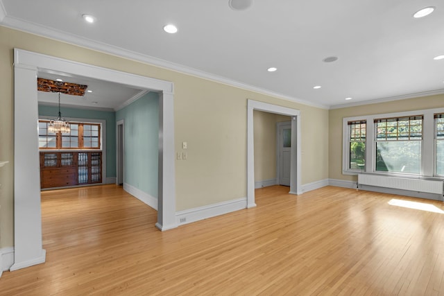 empty room featuring radiator, light wood-style flooring, ornamental molding, a chandelier, and baseboards
