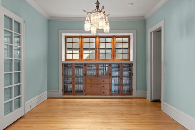 unfurnished dining area featuring a chandelier, wood finished floors, crown molding, and baseboards