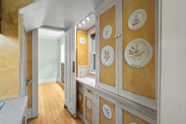 corridor with light wood-type flooring, ornamental molding, and baseboards
