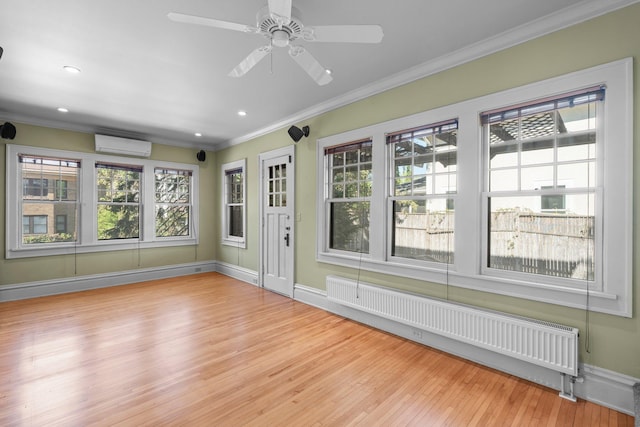 spare room featuring radiator heating unit, wood finished floors, ornamental molding, a wall unit AC, and baseboards