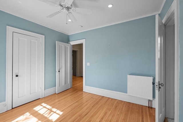 unfurnished bedroom featuring radiator heating unit, wood finished floors, crown molding, baseboards, and recessed lighting