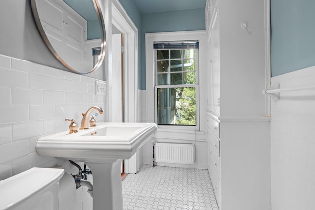 half bathroom featuring radiator, tile walls, a wainscoted wall, toilet, and tile patterned flooring