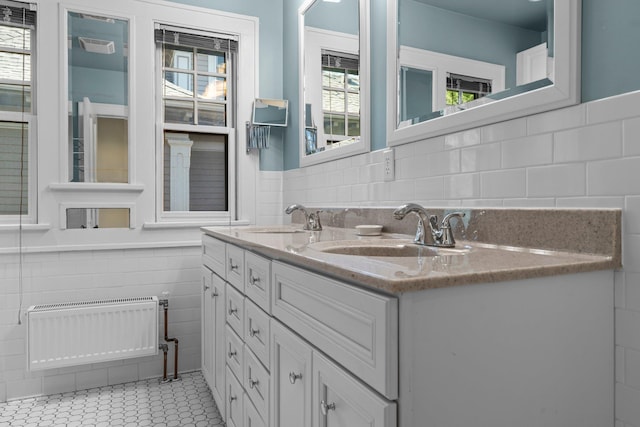 full bath with tile walls, radiator heating unit, a wainscoted wall, double vanity, and tile patterned floors